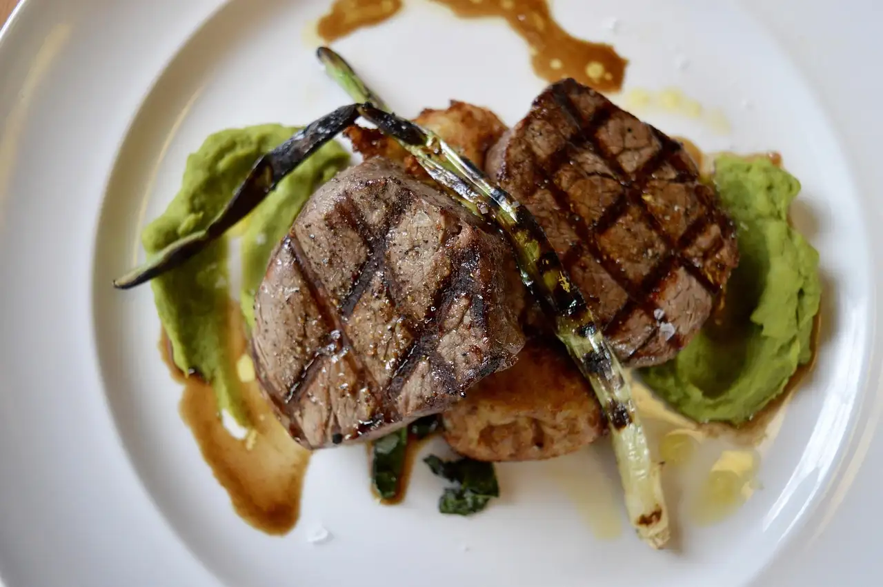 A plated grilled steak with green purée and charred spring onion on a white plate
