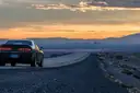 A car parked by a desert road at dusk, with the Las Vegas skyline and mountains in the distance