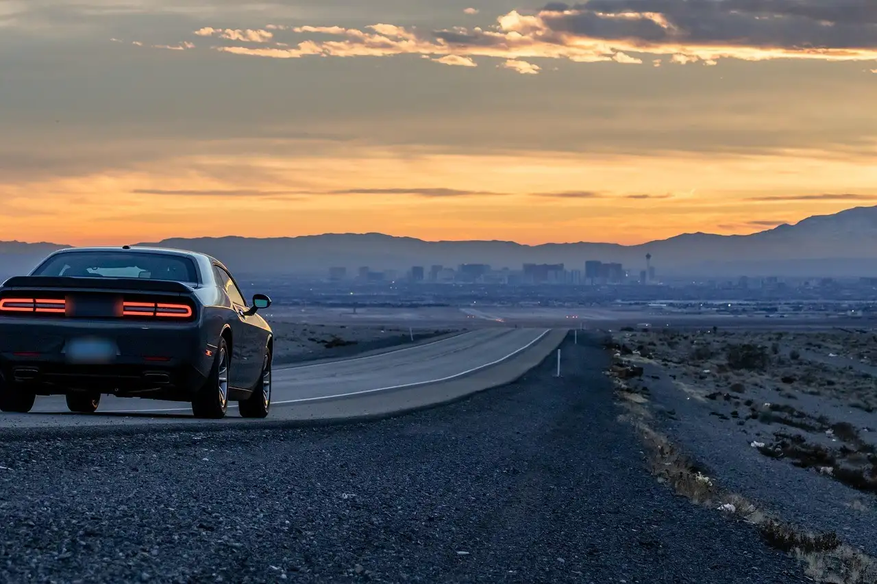 A car parked by a desert road at dusk, with the Las Vegas skyline and mountains in the distance