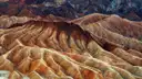 Folded badland ridges in brown, gold and cream, with dark mountains behind