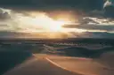 Sand dunes in low evening light under a cloudy sky with rays of sun