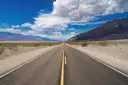 A straight desert road running toward mountains under a blue sky with white clouds