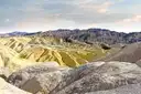 Rolling yellow and brown badlands in Death Valley below jagged mountains