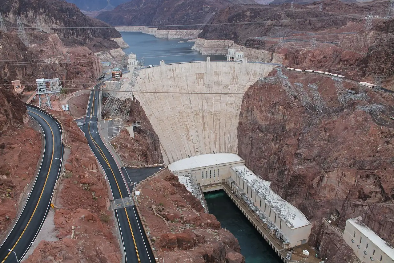 Hoover Dam from above, with the curved concrete wall, the power plant at its foot and Lake Mead behind