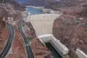 Hoover Dam from above, with the curved concrete wall, the power plant at its foot and Lake Mead behind