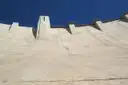 The curved concrete face of Hoover Dam rising to a tower against a deep blue sky