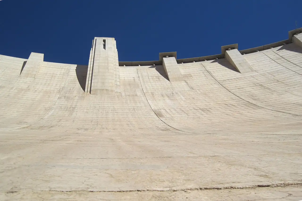 The curved concrete face of Hoover Dam rising to a tower against a deep blue sky