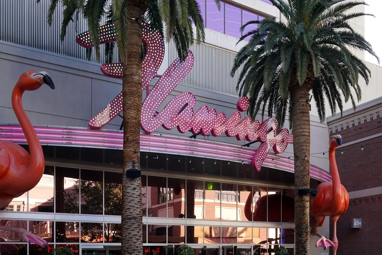 The pink script Flamingo sign and two flamingo statues among palm trees in Las Vegas