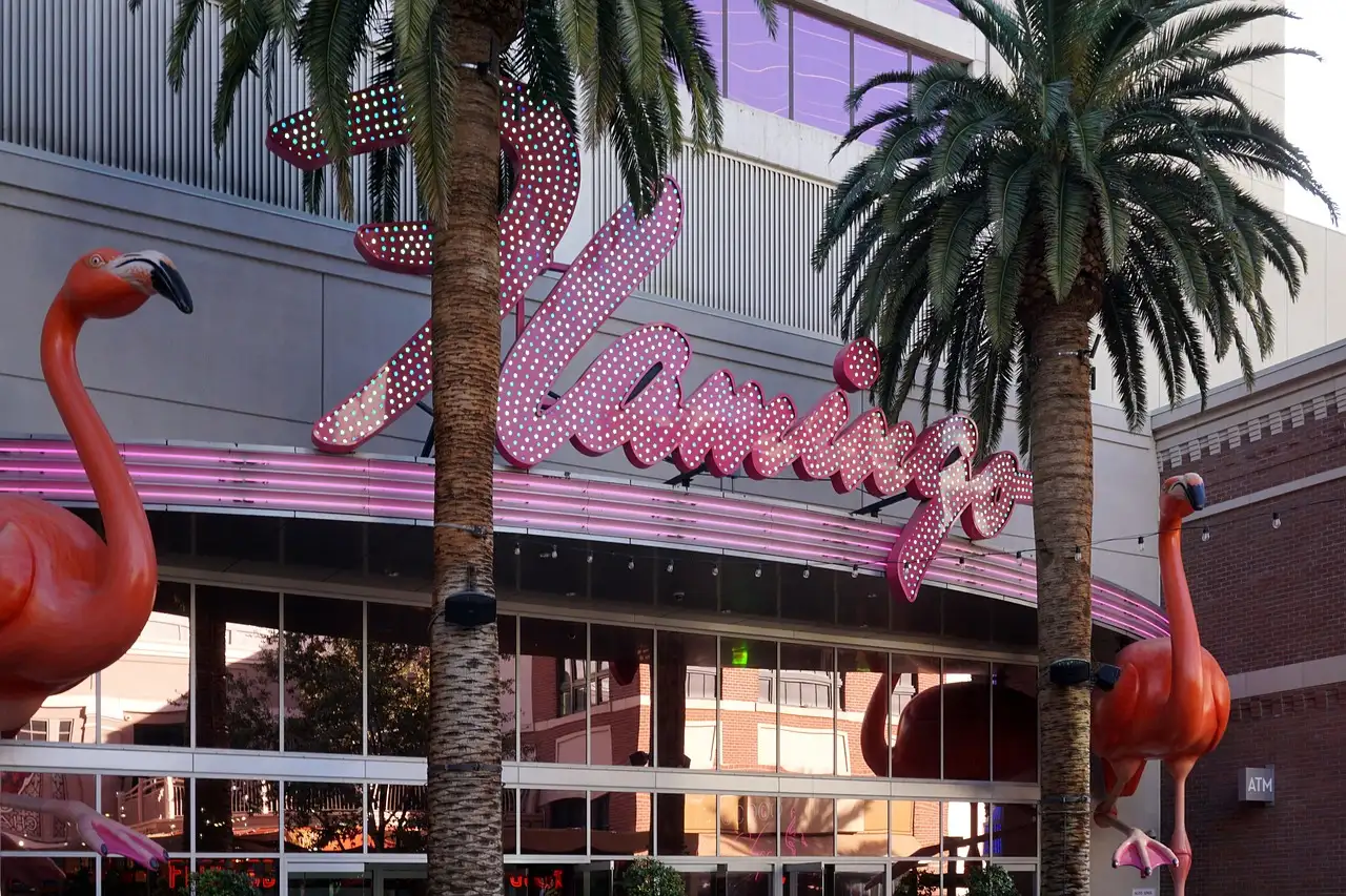 The pink script Flamingo sign and two flamingo statues among palm trees in Las Vegas