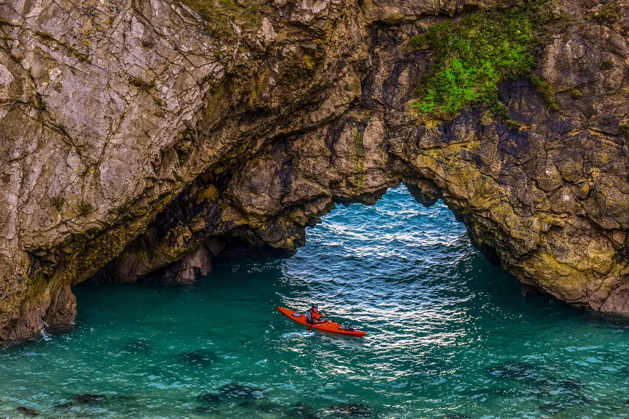 A red kayak paddling through a rock arch over clear turquoise water
