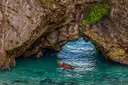 A red kayak paddling through a rock arch over clear turquoise water