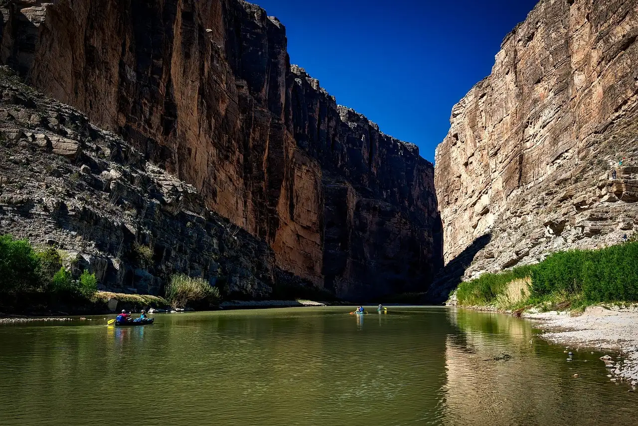 Small kayaks on a calm river between tall desert canyon walls