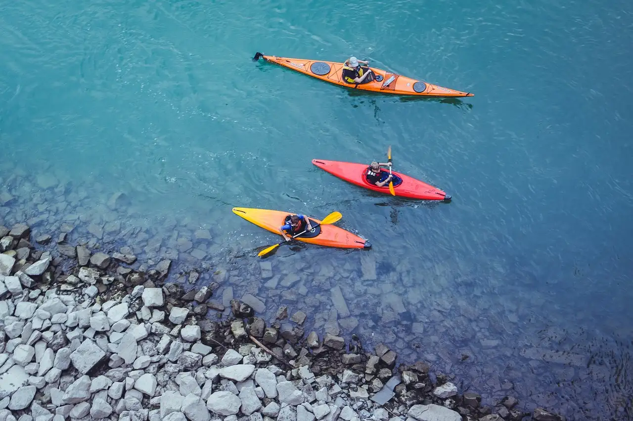 Three bright kayaks seen from above on clear blue-green water next to a rocky shore