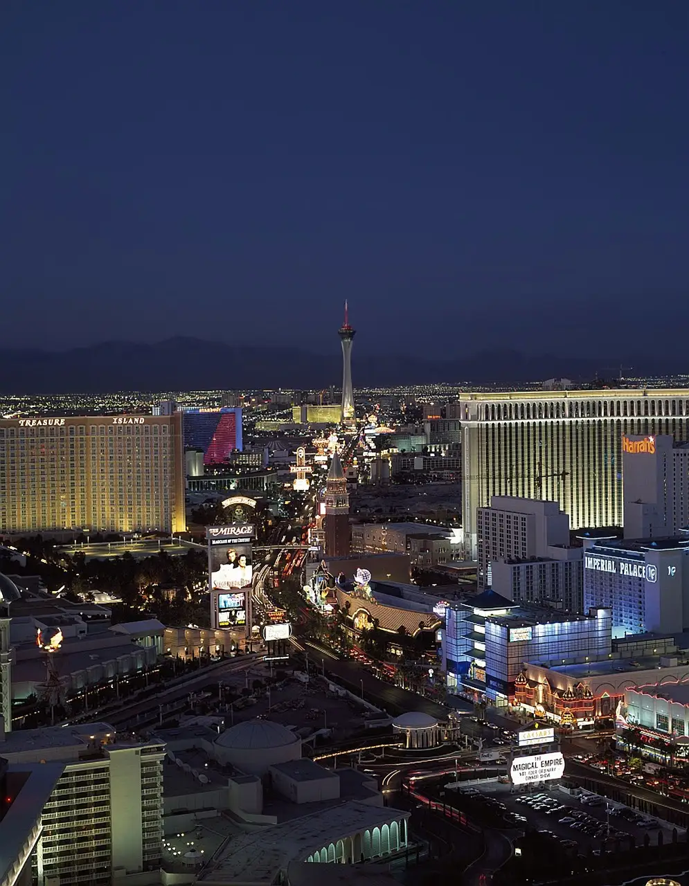 The Las Vegas Strip and the Strat tower from above at dusk, with the mountains behind the city