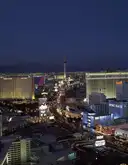 The Las Vegas Strip and the Strat tower from above at dusk, with the mountains behind the city