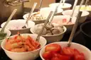 White bowls of shrimp, clams, tomatoes and salad with serving spoons on a buffet counter