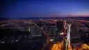 The Las Vegas Strip from the air at dusk, the STRAT tower lit white and the city lights running to the mountains