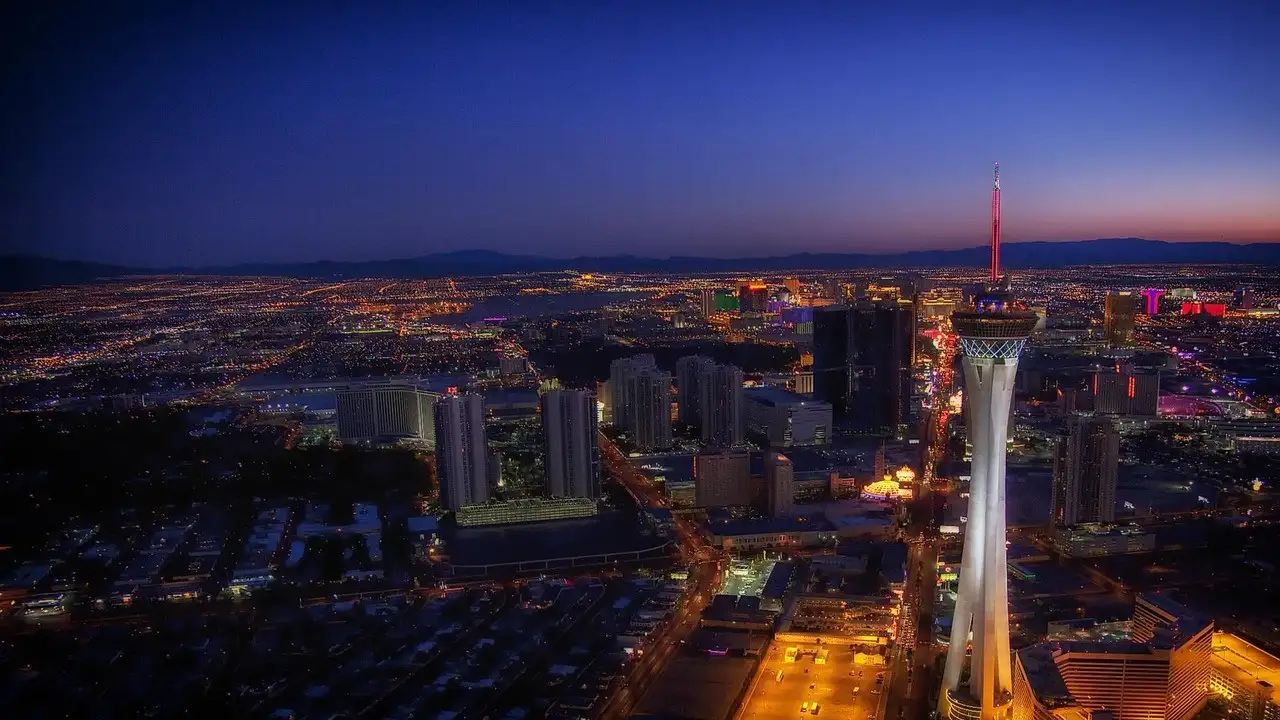 The Las Vegas Strip from the air at dusk, the STRAT tower lit white and the city lights running to the mountains