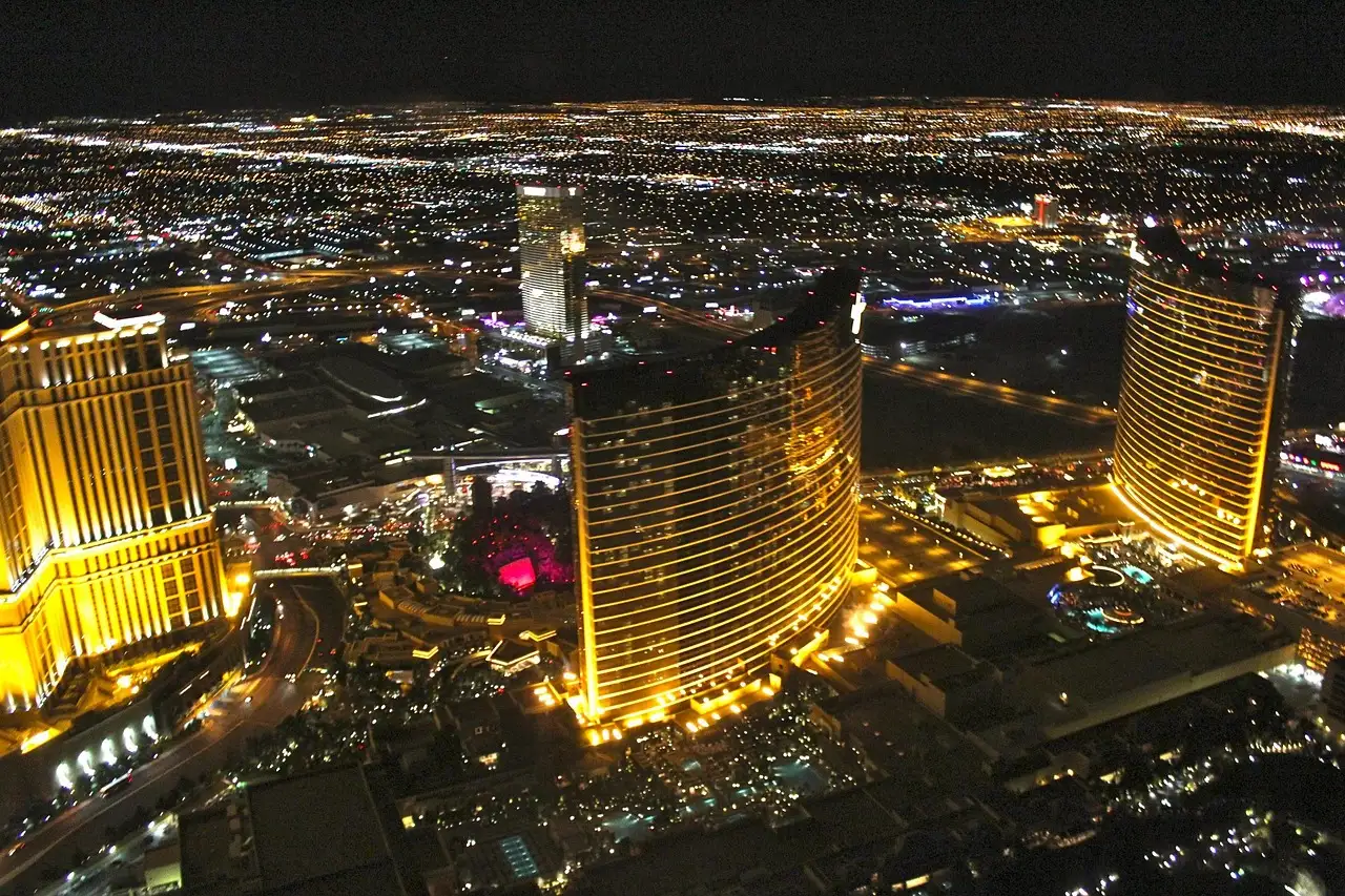 Gold-lit resort towers on the Las Vegas Strip at night, seen from the air, city lights to the horizon