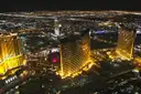 Gold-lit resort towers on the Las Vegas Strip at night, seen from the air, city lights to the horizon