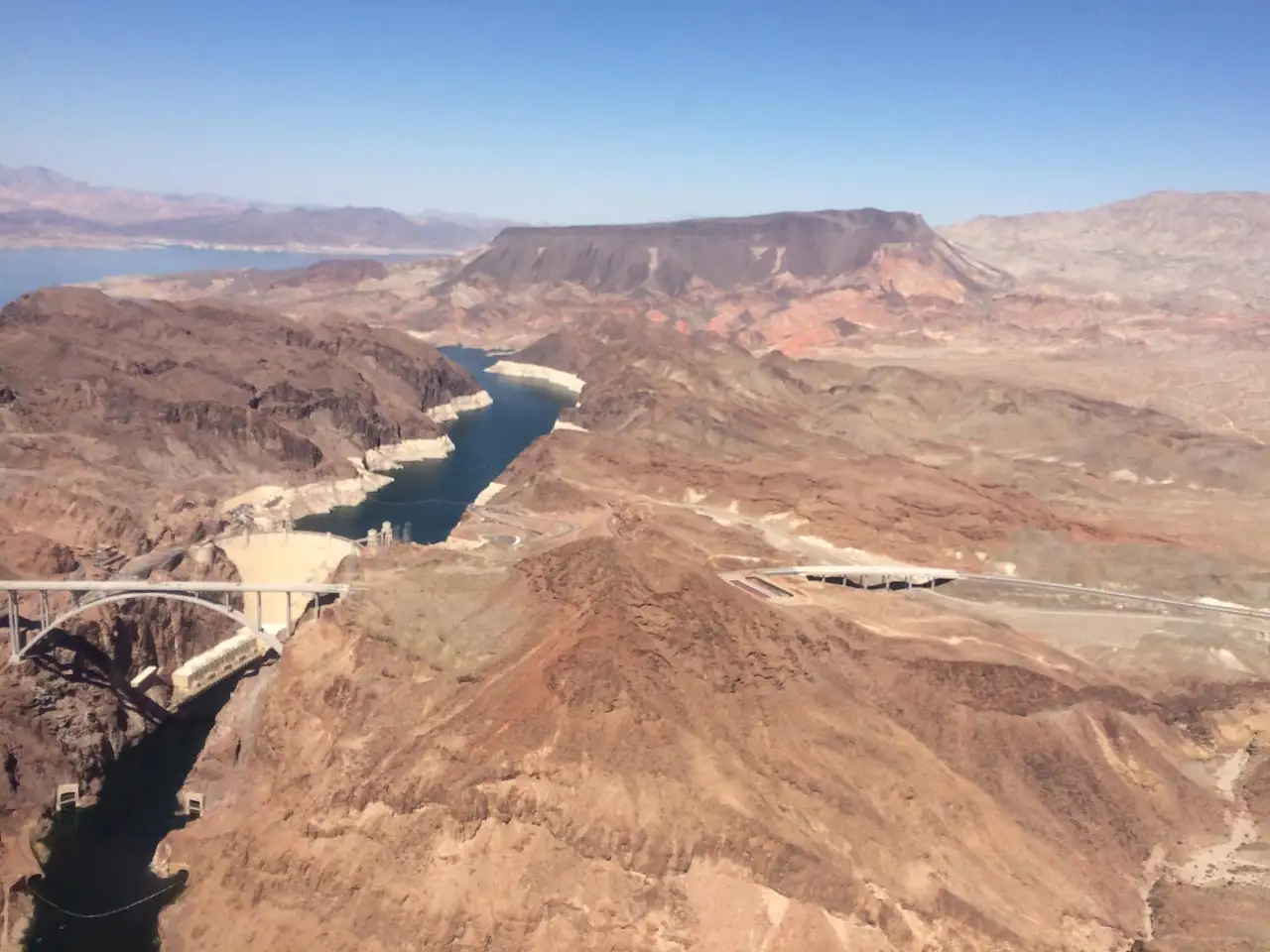 Air view of desert mountains with a lake, a dam and an arched bridge in the canyon
