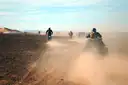 Riders in helmets kicking up dust on a desert track