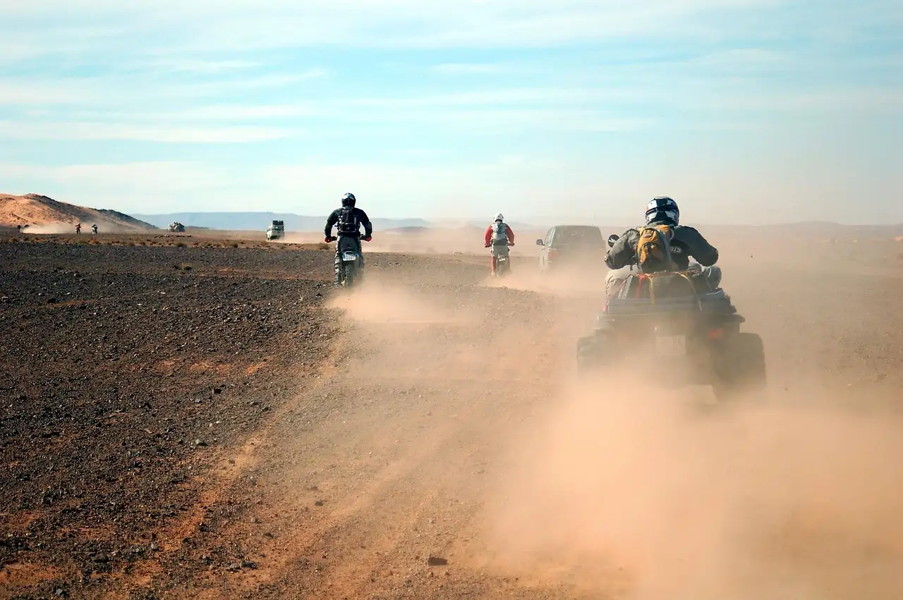 Riders in helmets kicking up dust on a desert track
