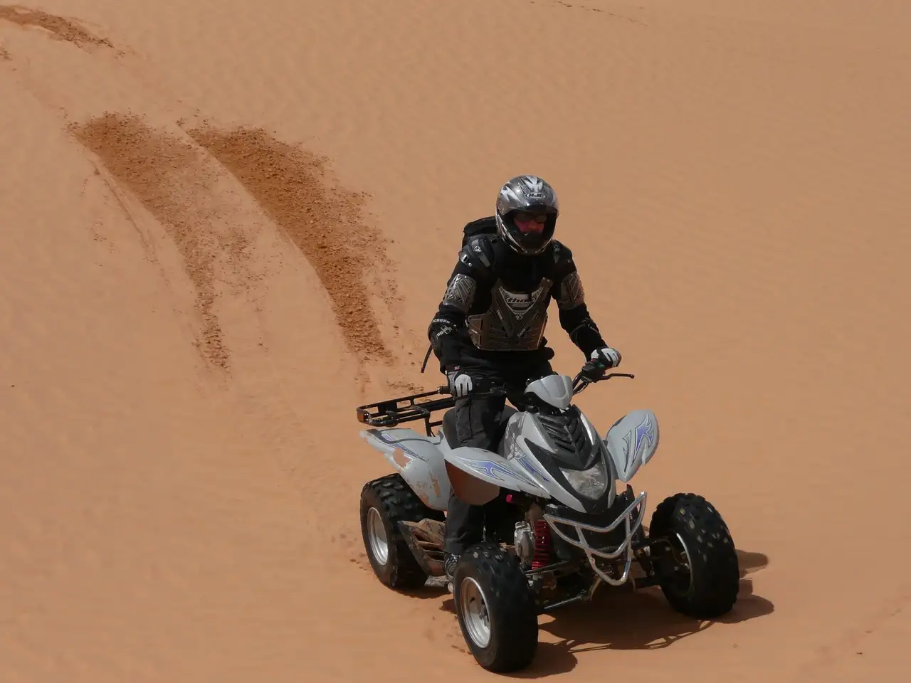 ATV rider in a helmet crossing orange sand dunes