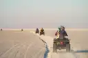 ATV riders seen from behind following a sandy track across flat desert