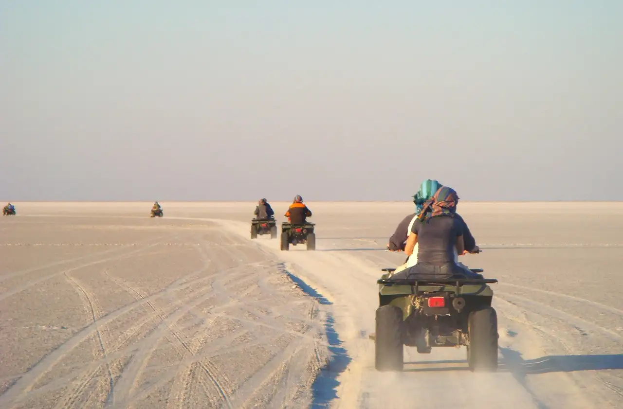 ATV riders seen from behind following a sandy track across flat desert