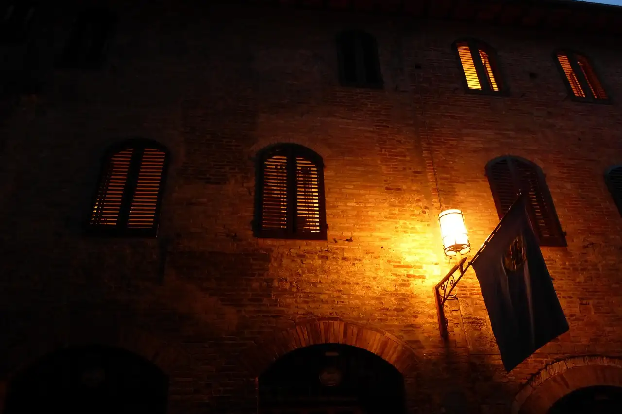 Old brick facade at night lit by a single wall lantern beside shuttered windows