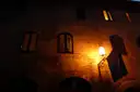 Old brick facade at night lit by a single wall lantern beside shuttered windows