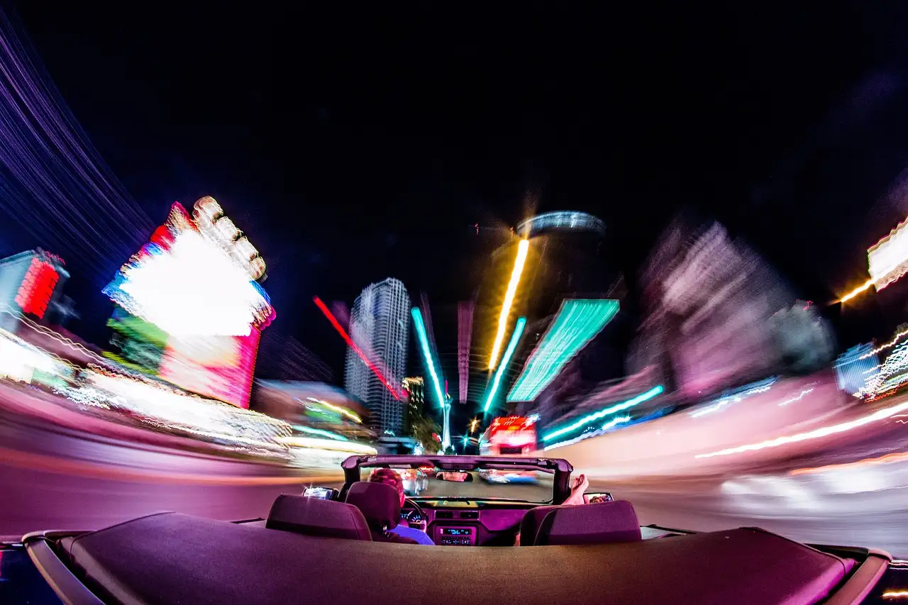 Open convertible driving down the Las Vegas Strip at night, neon lights blurred into streaks