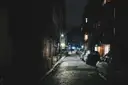Dark cobbled city street at night with parked cars and distant street lamps