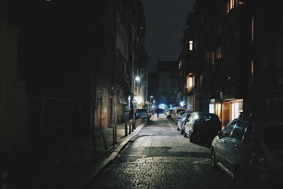 Dark cobbled city street at night with parked cars and distant street lamps