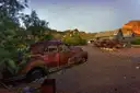 Rusted old car beside tin-roofed sheds in a desert canyon at dusk