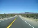 Two-lane desert highway between Joshua trees toward flat-topped cliffs