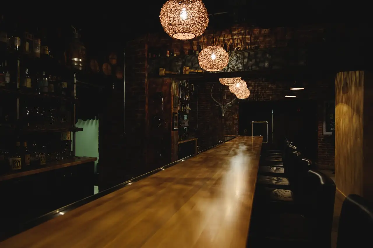 Long empty wooden bar counter in a dark brick bar lit by woven pendant lamps