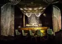 Dim, empty lounge bar with green velvet stools, a glowing gold counter and hanging chain curtains