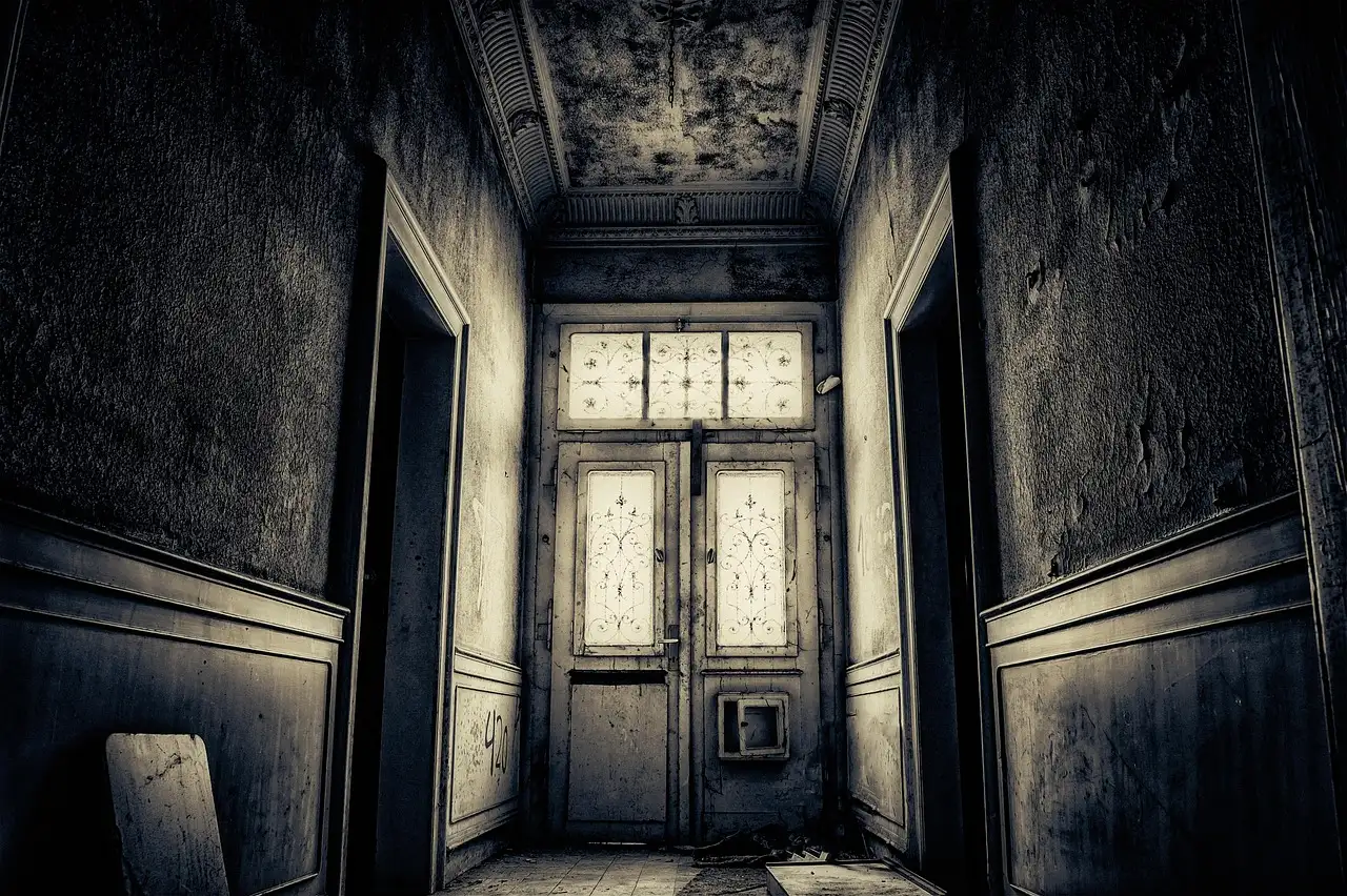 Dim, decaying old corridor with peeling walls leading to a glass-paneled double door