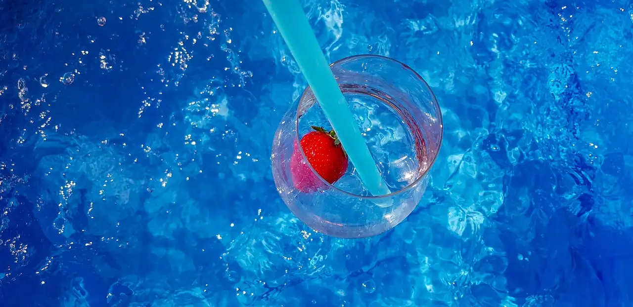 Drink with a strawberry and blue straw against pool water