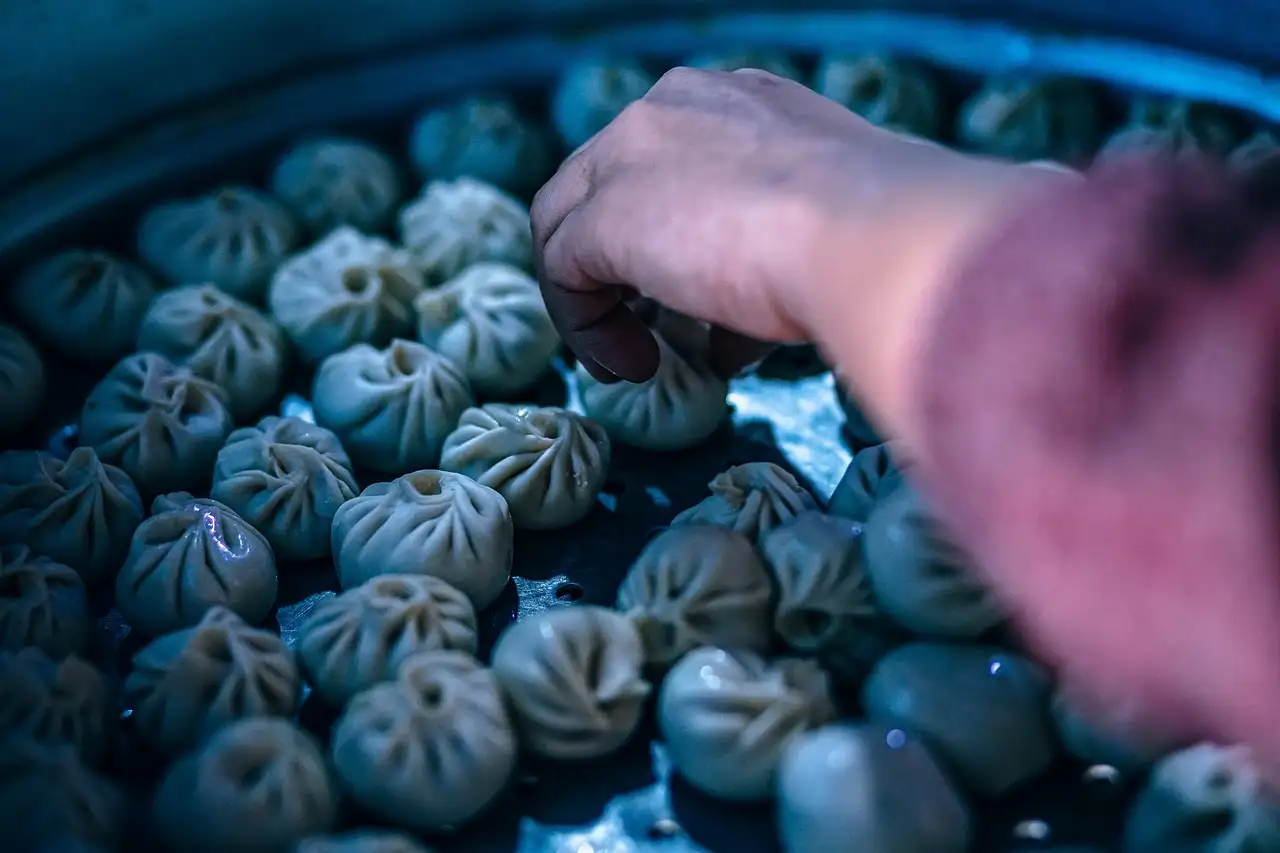 Hand picking a dumpling from a tray of steamed dumplings