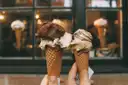 Two hands holding gelato cones in front of a shop window