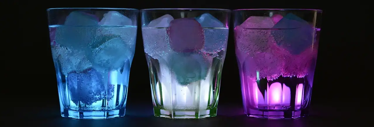 Three glasses with ice glowing blue, white and purple