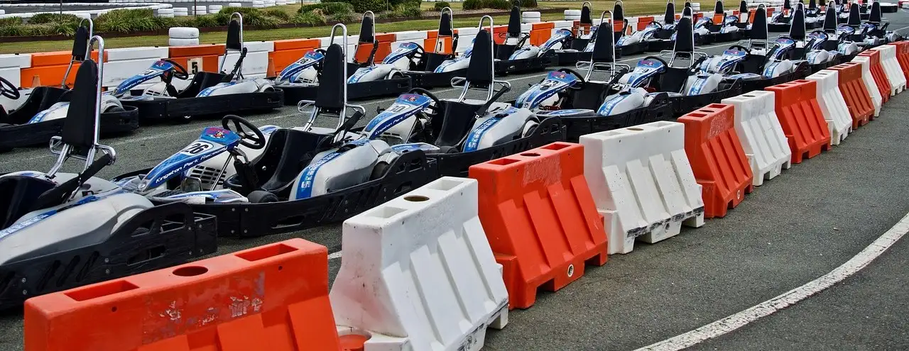 Rows of empty go-karts lined up behind orange and white barriers at an open-air track