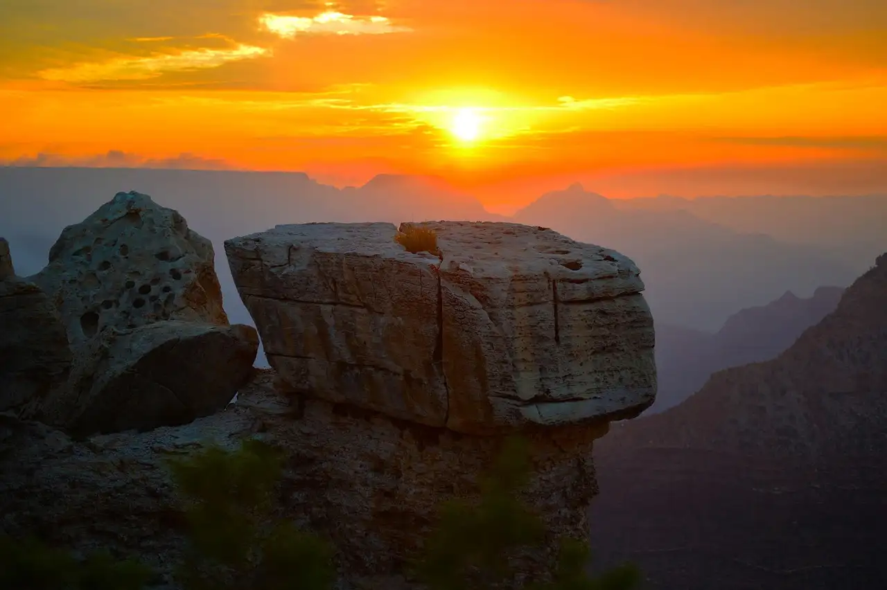 Sun setting over the canyon in an orange sky, a flat rock in front