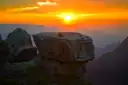 Sun setting over the canyon in an orange sky, a flat rock in front