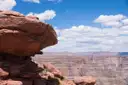 Red rock outcrop on the rim with the layered canyon beyond under white clouds