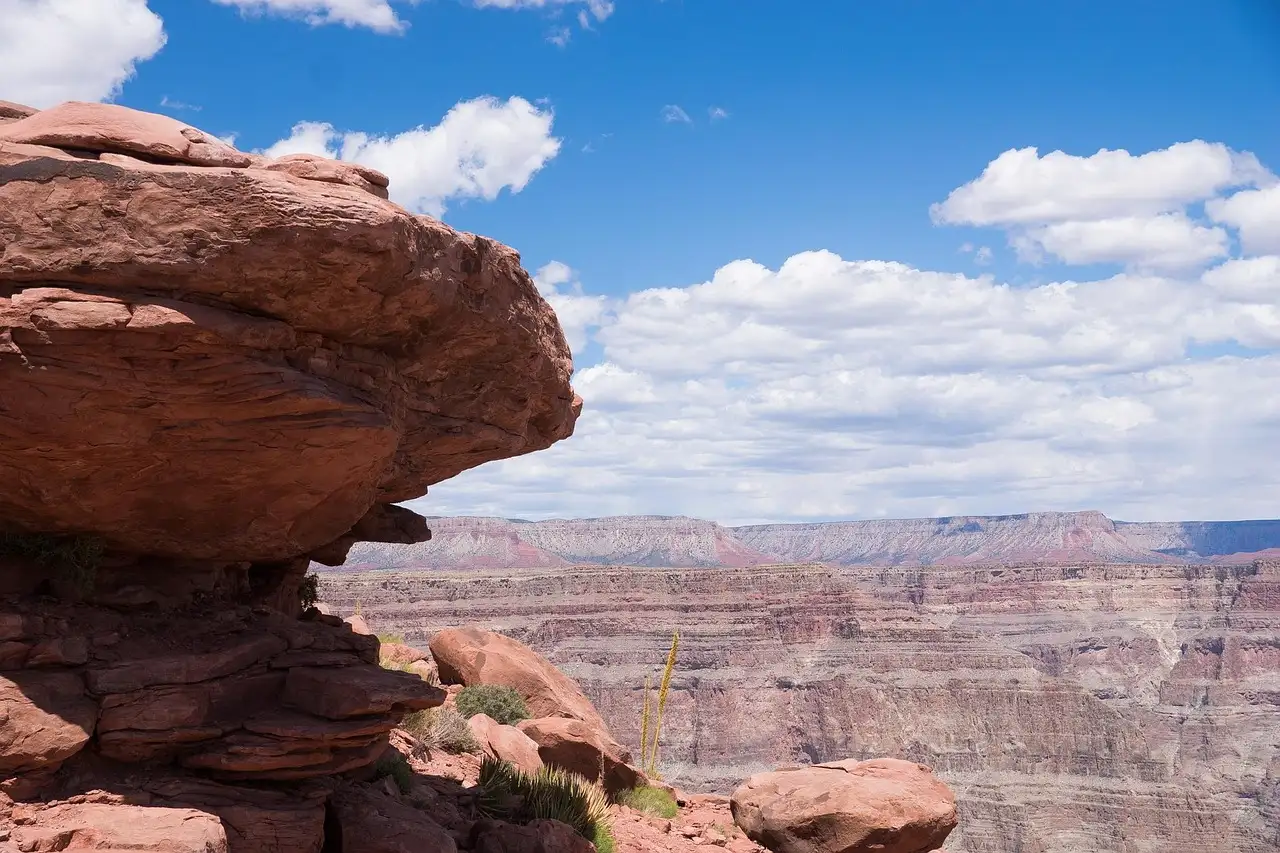 Red rock outcrop on the rim with the layered canyon beyond under white clouds