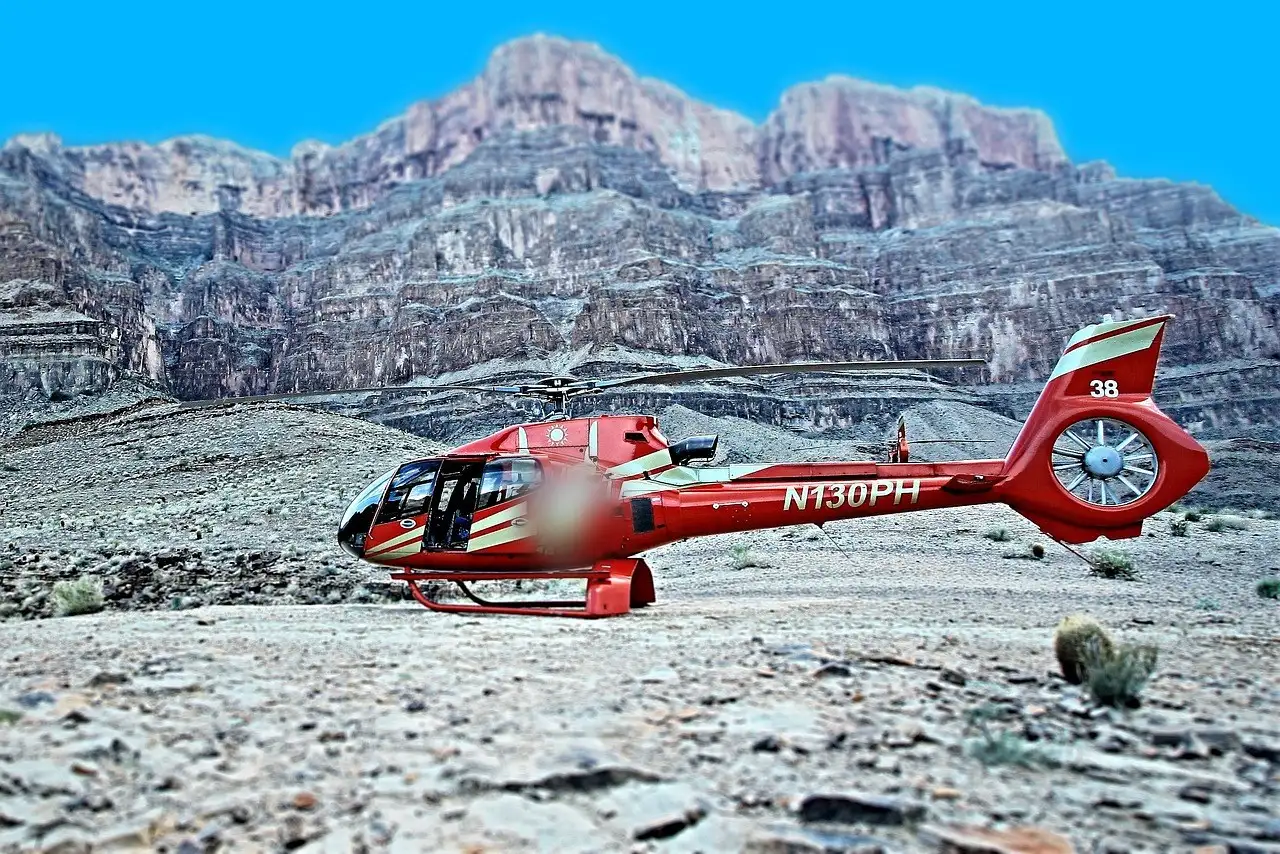 Red helicopter parked on a rocky canyon floor below tall cliffs